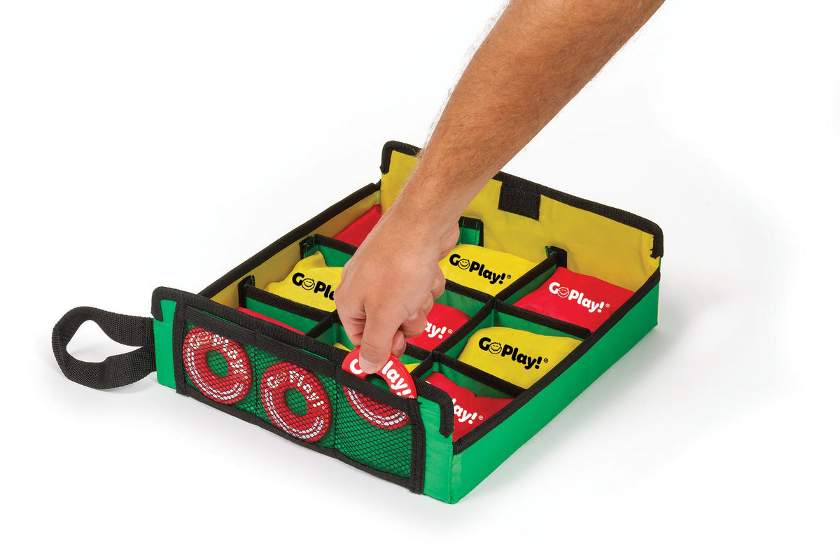 A hand placing a red washer into the target’s mesh storage pocket, with bean bags arranged in the tic tac toss grid